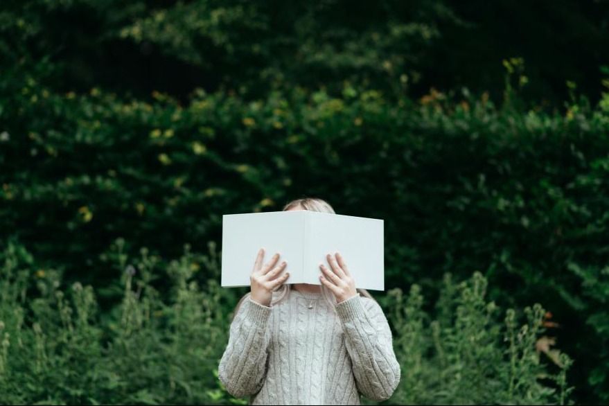 woman hiding behind a book in nature