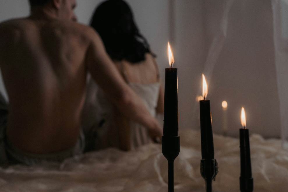 A couple on a bed with candles lit in the background 